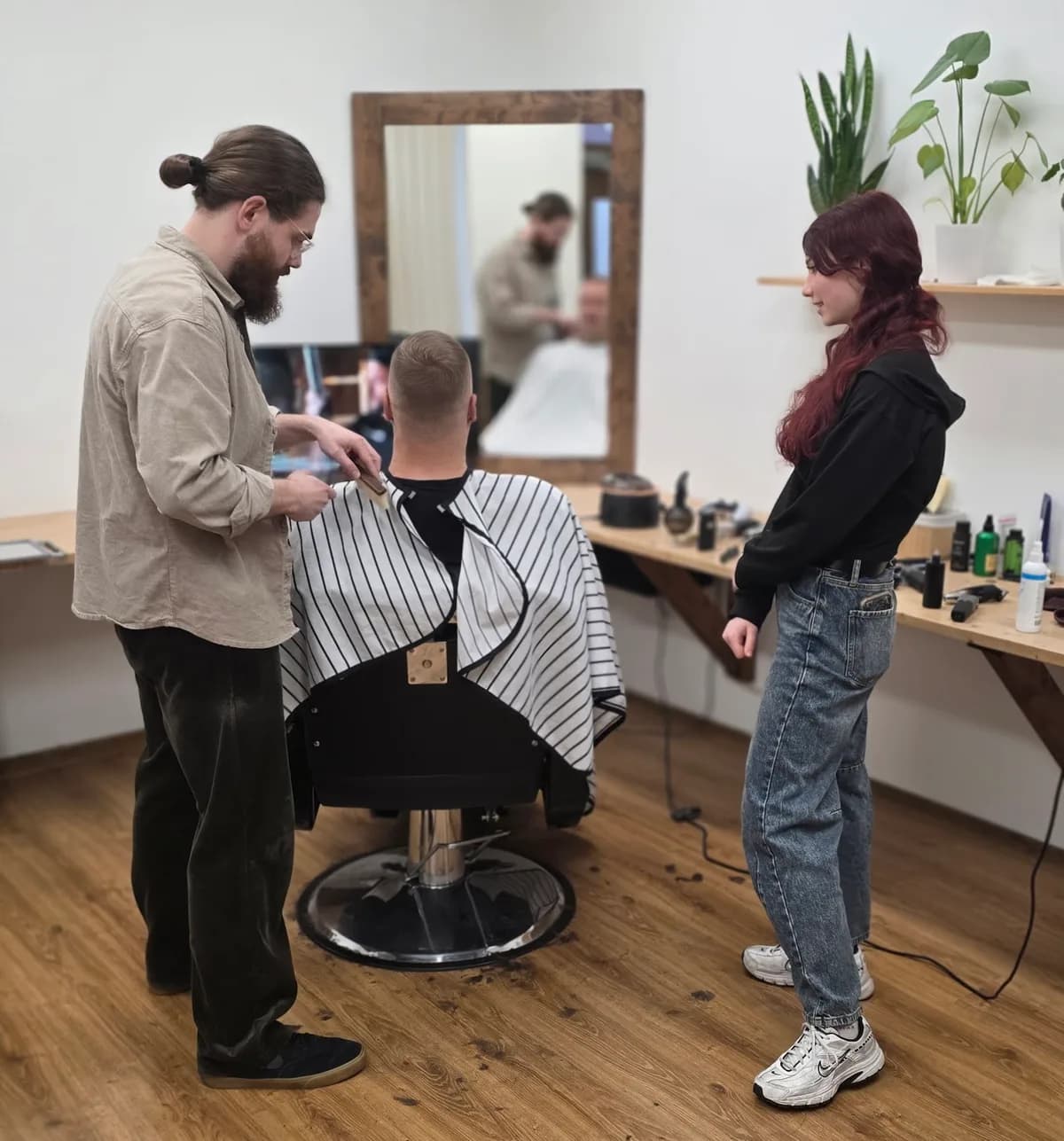 Эрмо стрижёт клиента, а Ира следит за работой в салоне Barbermo